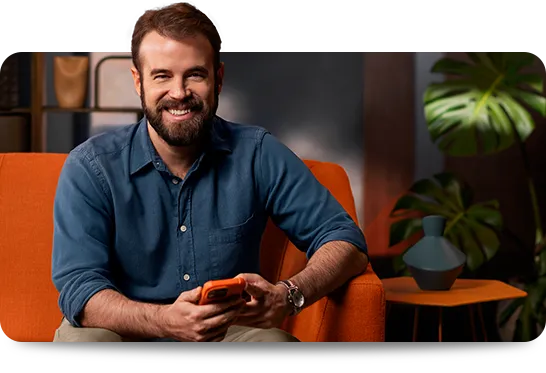 Homem sentado, sorrindo e segurando um celular