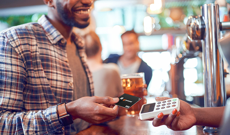 Homem sorrindo enquanto entrega seu cartão pré-pago da Conta Digital da Efí para realizar o pagamento pelo consumo em uma chopperia.