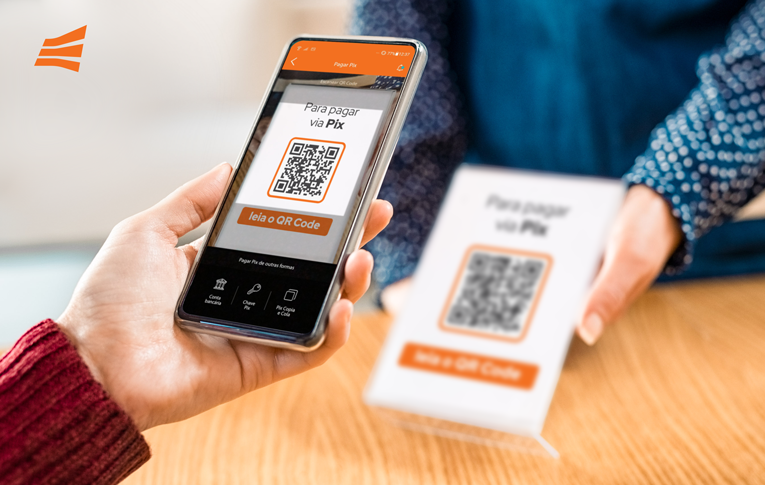 Comerciante segura a plaquinha com QR Code Pix para PJ impresso, enquanto o pagador utiliza o smartphone para realizar o pagamento via Pix
